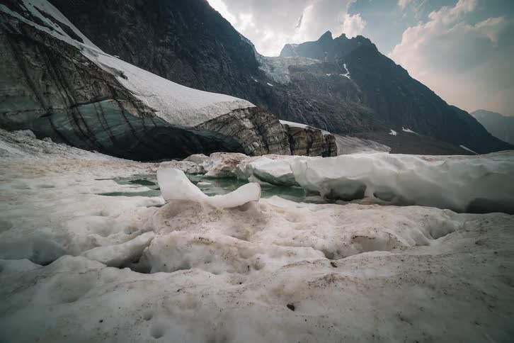 Dramatic timelapse of clouds moving over a rugged mountain range and a vast, melting glacier