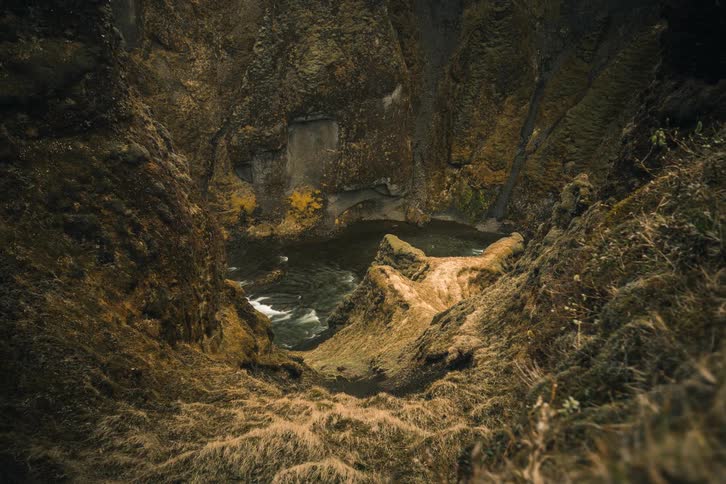 A moody time-lapse from above reveals a dark river flowing through a deep and rugged moss-covered canyon