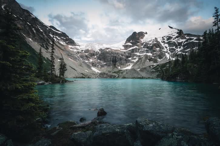 A dramatic time-lapse reveals a pristine glacial lake surrounded by majestic snow-capped mountains as clouds roll by