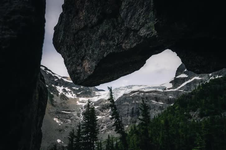 A dramatic dolly shot reveals a beautiful mountain valley and glacier framed by large rocks
