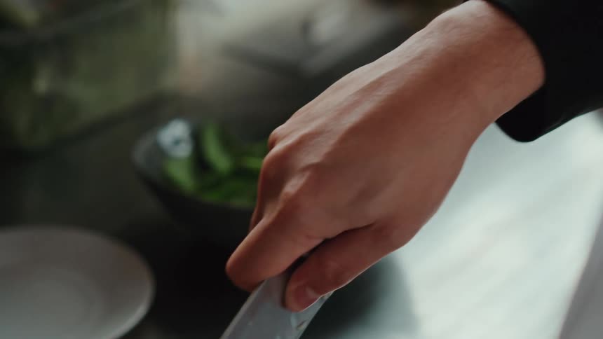 A professional chef sprinkles seasoning before meticulously chopping green onions in a slow-motion close-up