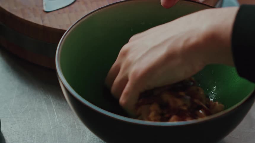 Close up slow motion shot of a cook pouring soy sauce over chopped meat and mixing the marinade by hand