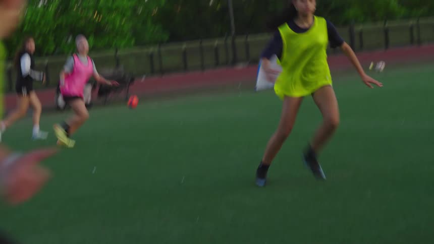 Dynamic slow-motion footage follows female soccer players as they practice drills on a city field at dusk
