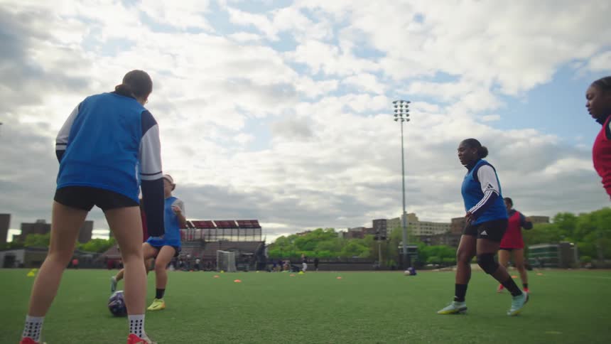 A diverse group of female athletes participates in a soccer training drill in slow motion on a city field