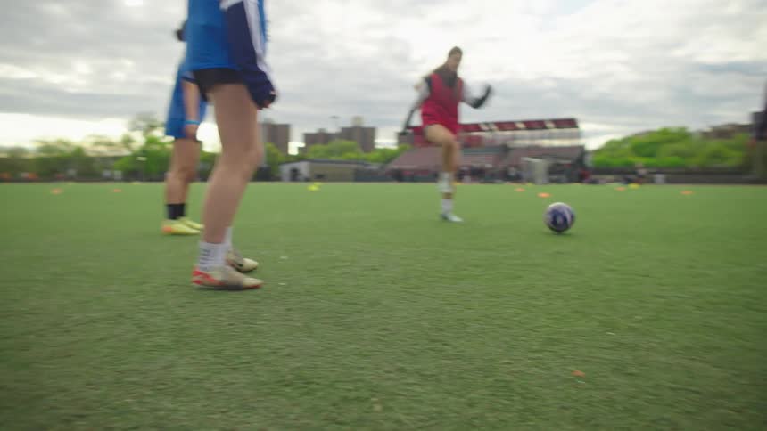 Slow motion low-angle of a diverse group of female soccer players practicing passing drills on an urban turf field