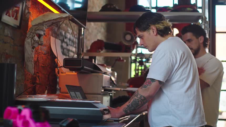 Two men work together in a creative design studio, operating a large format printer for a project