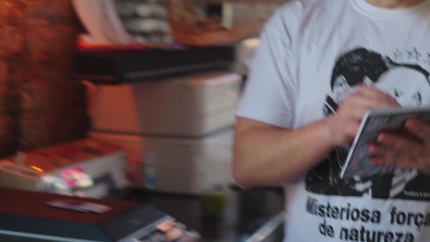 A tattooed artist with a mullet carefully packages printed materials in his creative workshop
