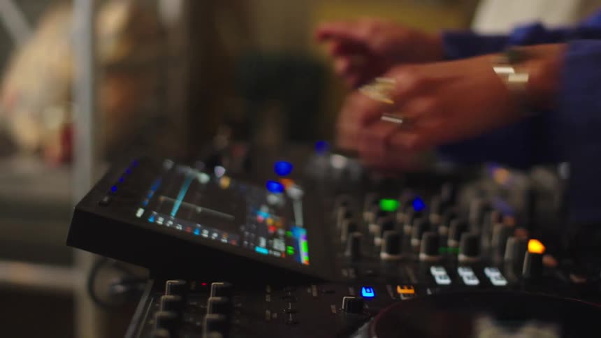 A slow-motion close-up reveals a DJ's hands skillfully manipulating the knobs and faders of a professional mixing console