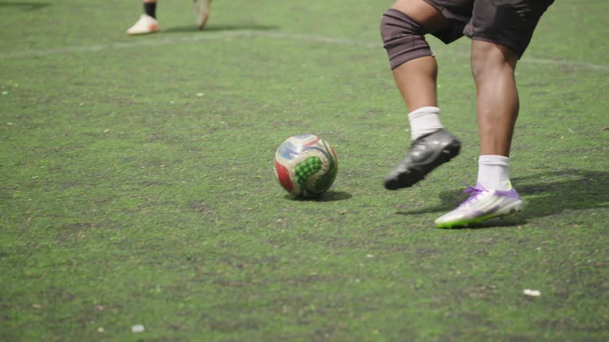 In super slow motion, a soccer player skillfully dribbles the ball down the turf field during a pickup game in an urban park
