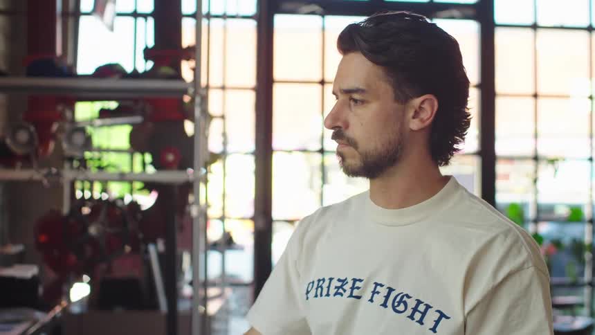 A focused artisan uses a heat press machine to apply a custom design to a garment in his sunlit workshop