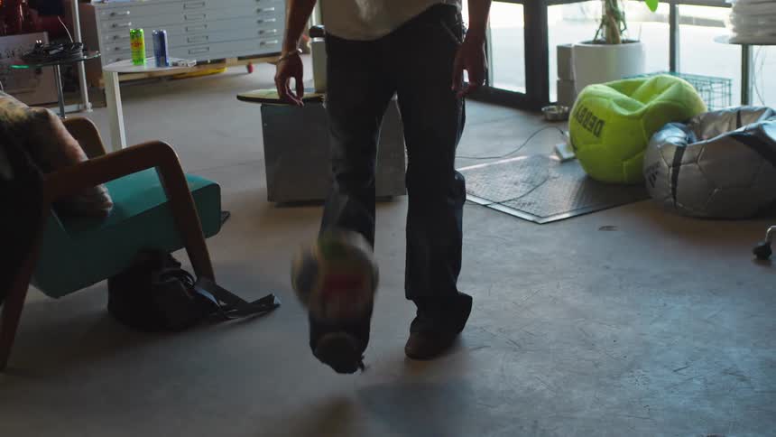 A cool young man skillfully juggles a soccer ball in slow motion inside a sunlit creative studio