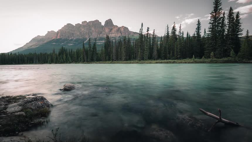 A serene time-lapse of a smooth-flowing river in a forest valley with a majestic mountain range in the background
