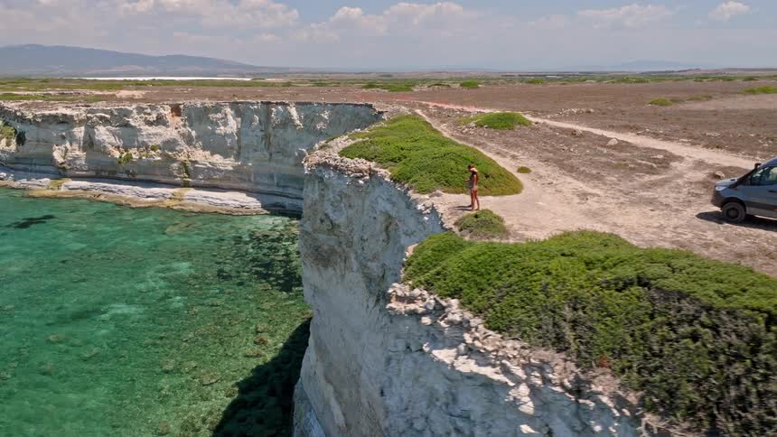 Aerial view of an adventurous couple on a camper van road trip stopping to admire the breathtaking view from a high cliff over the turquoise sea