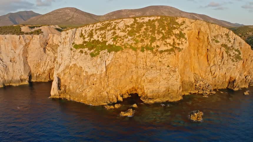 A serene aerial shot captures the golden hour light on a rugged, rocky coastline with deep blue waters