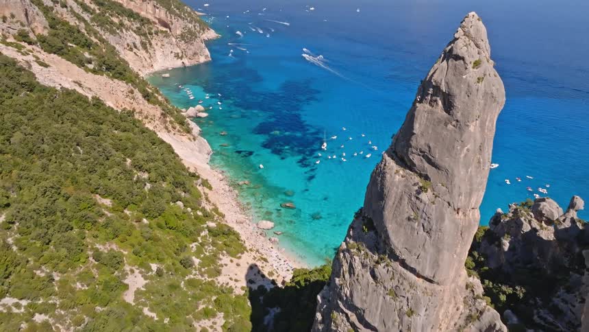 Stunning aerial reveal of the famous Aguglia rock pinnacle at Cala Goloritzé, showcasing the crystal-clear turquoise waters and coastline of Sardinia
