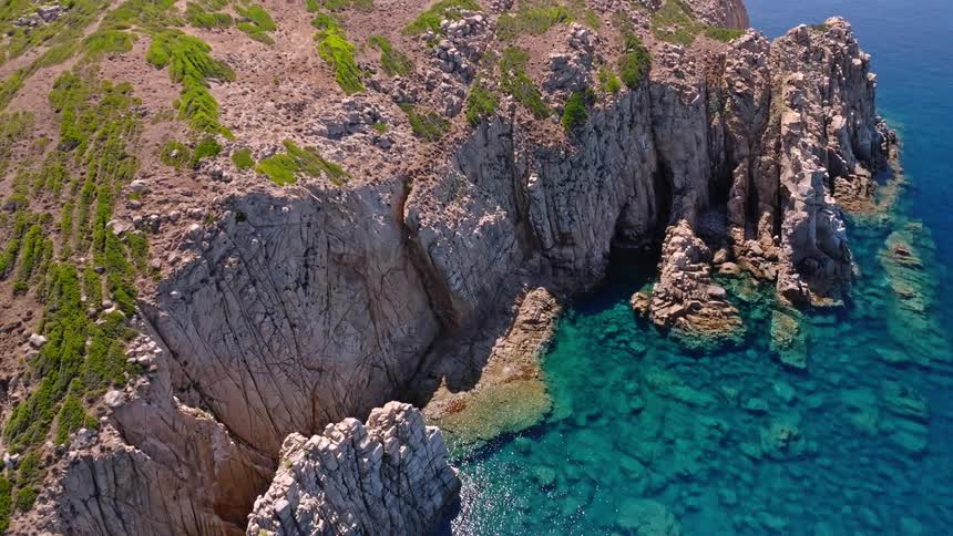 A stunning aerial shot pulls back from a rocky cliff to reveal the breathtaking turquoise sea along a rugged coastline