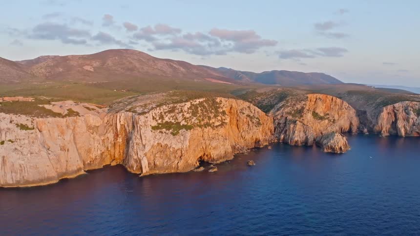 Breathtaking aerial view of the dramatic rocky coastline of Sardinia, Italy, with cliffs glowing in the golden light of sunset