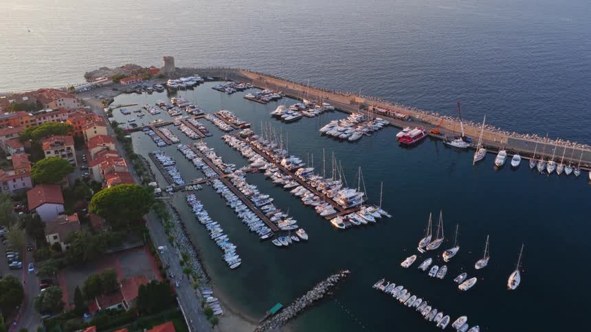 A beautiful aerial shot slowly moves over the scenic harbor of Marciana Marina on the island of Elba, Italy, during a calm sunrise