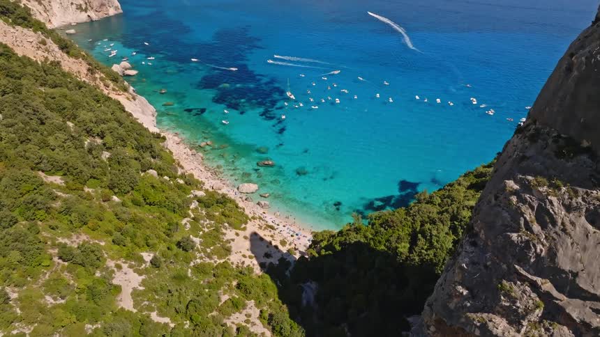 A majestic aerial view of the iconic Aguglia rock pinnacle overlooking the stunning turquoise bay and beach of Cala Goloritze, Sardinia