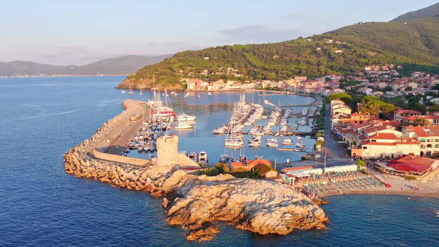 Stunning aerial footage captures the picturesque Marciana Marina on the island of Elba, Italy, with its harbor full of boats bathed in golden sunrise light
