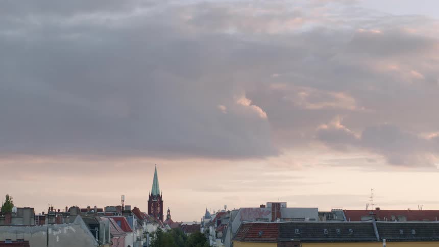 A peaceful European city skyline with a prominent church steeple under a beautiful sky of soft, rolling clouds at sunset
