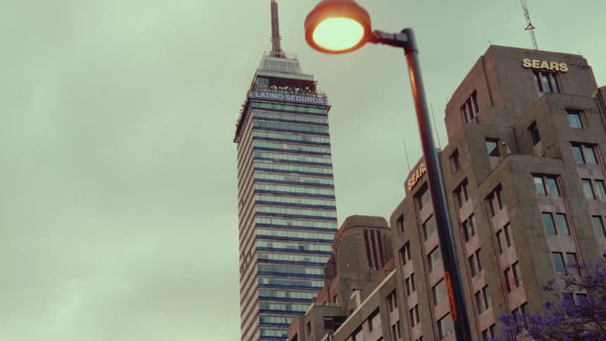 Slow dolly shot past a glowing street lamp with the iconic Torre Latinoamericana skyscraper in the background on an overcast day in Mexico City