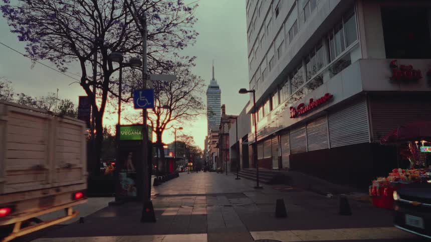 An atmospheric slow-motion shot of a city street at sunset with the Torre Latinoamericana in the distance