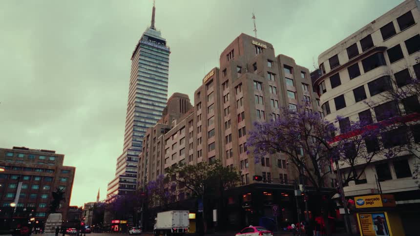 A slow pan reveals the iconic Torre Latinoamericana skyscraper amidst the evening traffic and historic buildings of downtown Mexico City
