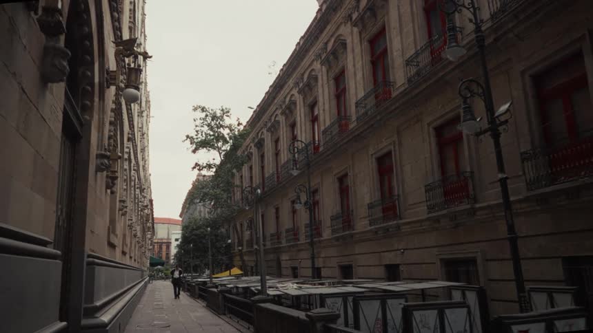 A man in a suit walks in slow motion down a deserted city alleyway lined with ornate historical buildings and closed market stalls
