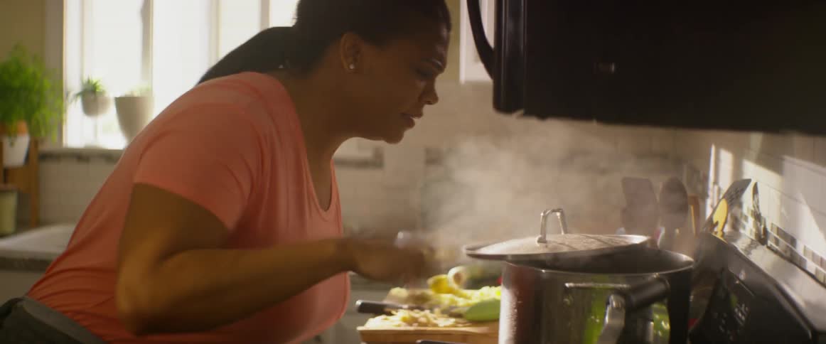 A woman burns her hand while lifting a hot lid in the kitchen