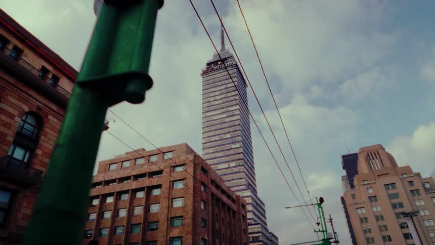 A cinematic low-angle dolly shot pushes past a street light to reveal the iconic Torre Latinoamericana skyscraper in downtown Mexico City