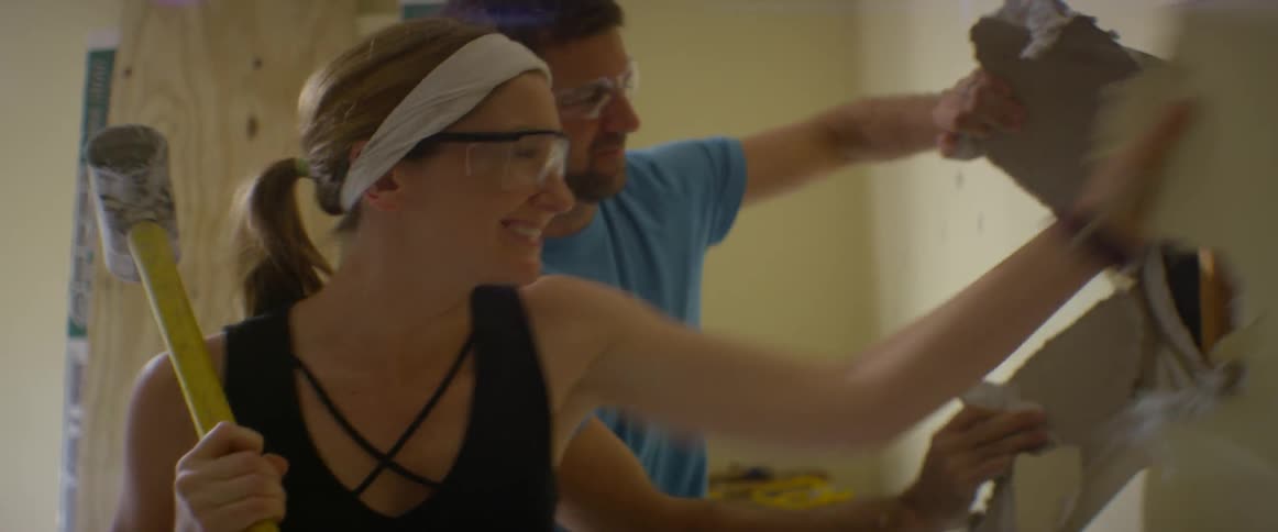 Man and woman use sledgehammer to break drywall