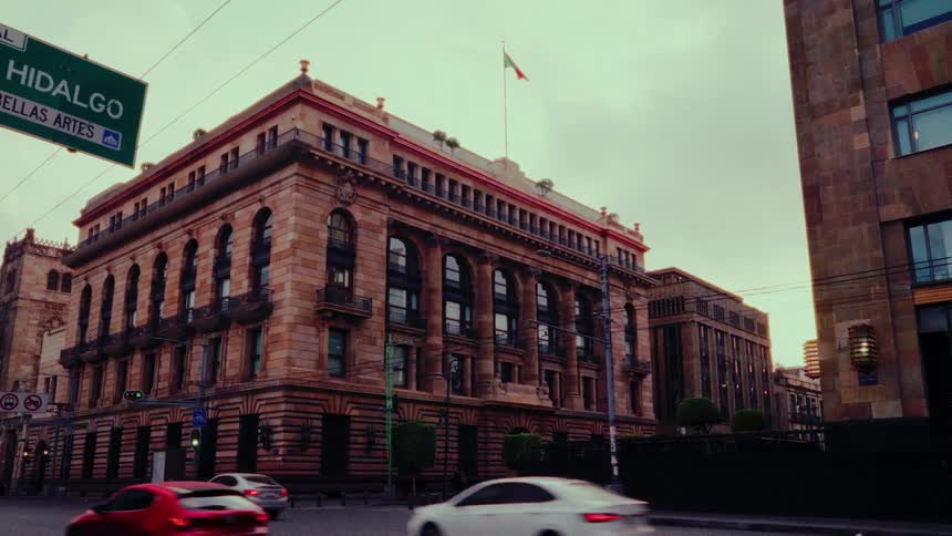A low-angle shot tilts up from street-level traffic to reveal the historic Banco de Mexico building in Mexico City at dusk
