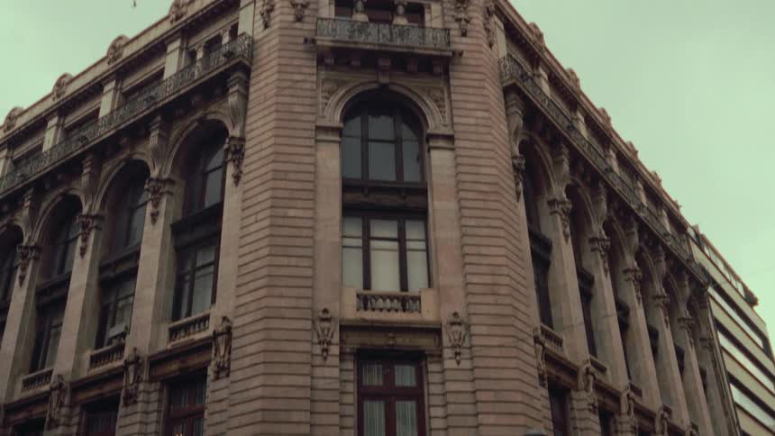 Tilting up from a city street corner to reveal the grand, classical architecture of a historic building with a clock tower