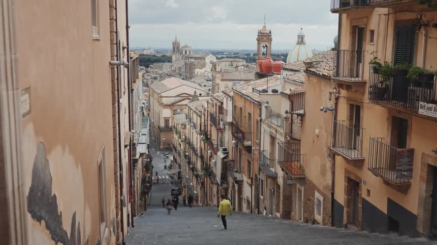A lone person walks down a long historic staircase in the charming Italian city of Caltagirone on a cloudy day