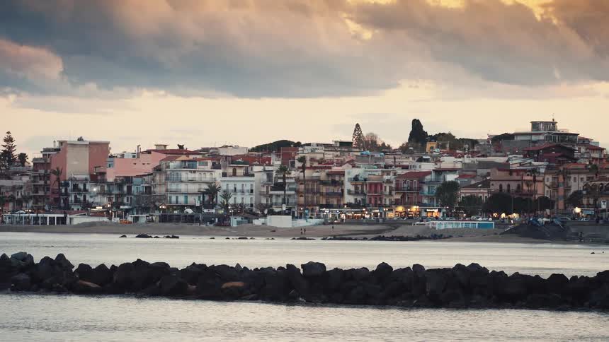 A tranquil evening view of the illuminated coastal town of Giardini Naxos, Sicily, from across the bay