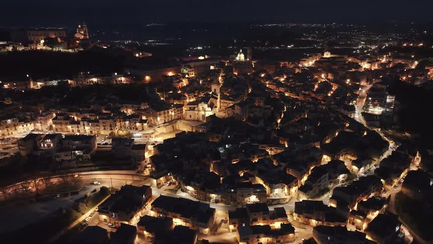 A slow-pullback aerial shot reveals the enchanting glow of a historic European city illuminated at night