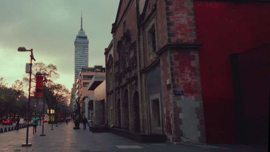 A jogger runs past a historic building on a quiet Mexico City street at dusk, with the iconic Torre Latinoamericana skyscraper in the background