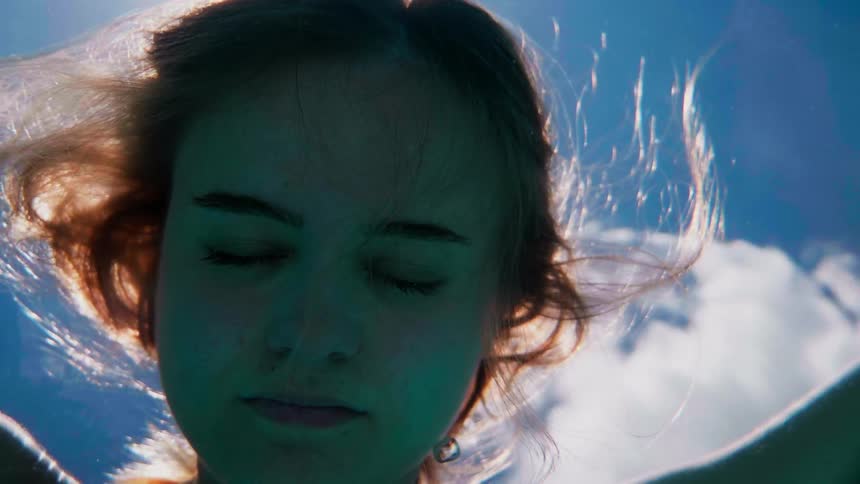A woman with her eyes closed floats face down in water