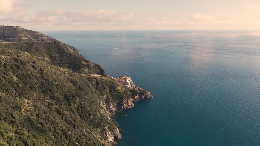 A stunning aerial view flies over the terraced hills of the Italian Riviera, revealing the cliffside village of Cinque Terre against the vast blue sea