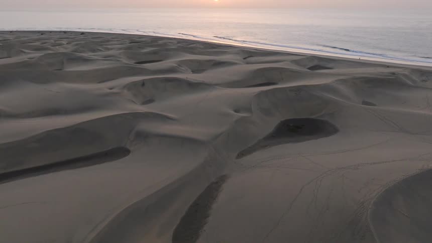 An epic aerial tilt reveals a beautiful sunrise over vast coastal sand dunes and the ocean