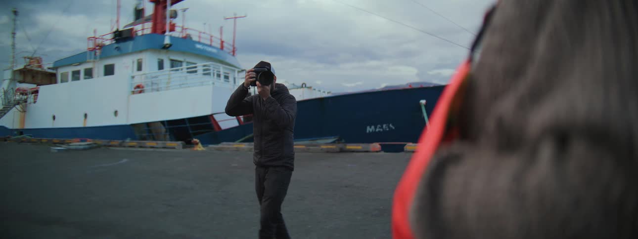 Over-the-shoulder slow motion shot of a man taking a picture with his camera at a shipping port