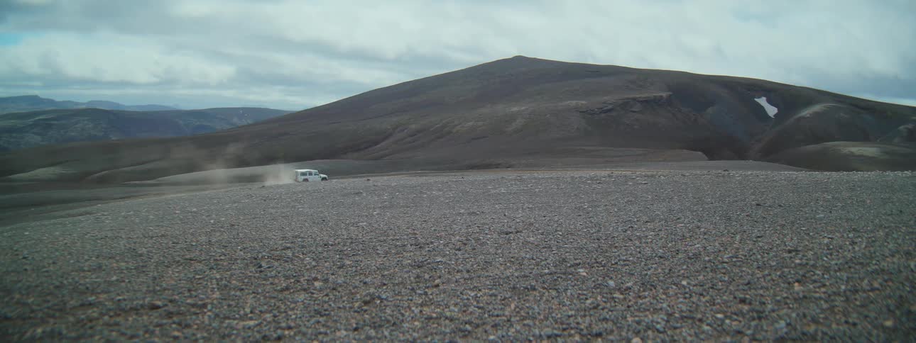 A white off-road expedition vehicle kicks up dust as it drives across a vast and desolate rocky plain
