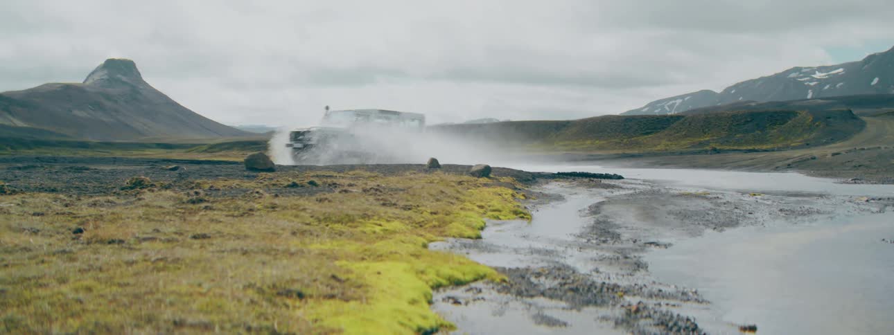 An adventurous white SUV splashes through a shallow river while off-roading through a vast, mossy landscape