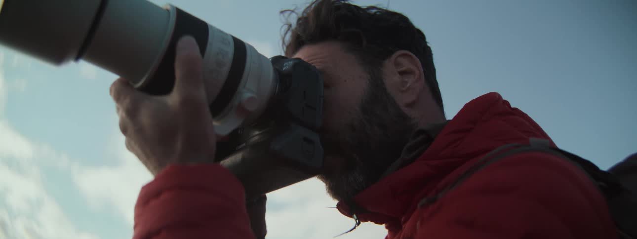 Close-up of a male photographer with a beard raising his camera with a large telephoto lens to take a picture