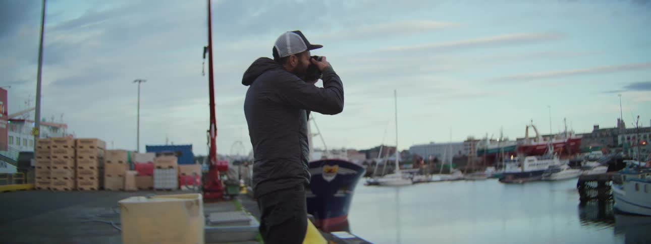 A male photographer in slow motion captures scenic shots of a busy industrial harbor at dusk