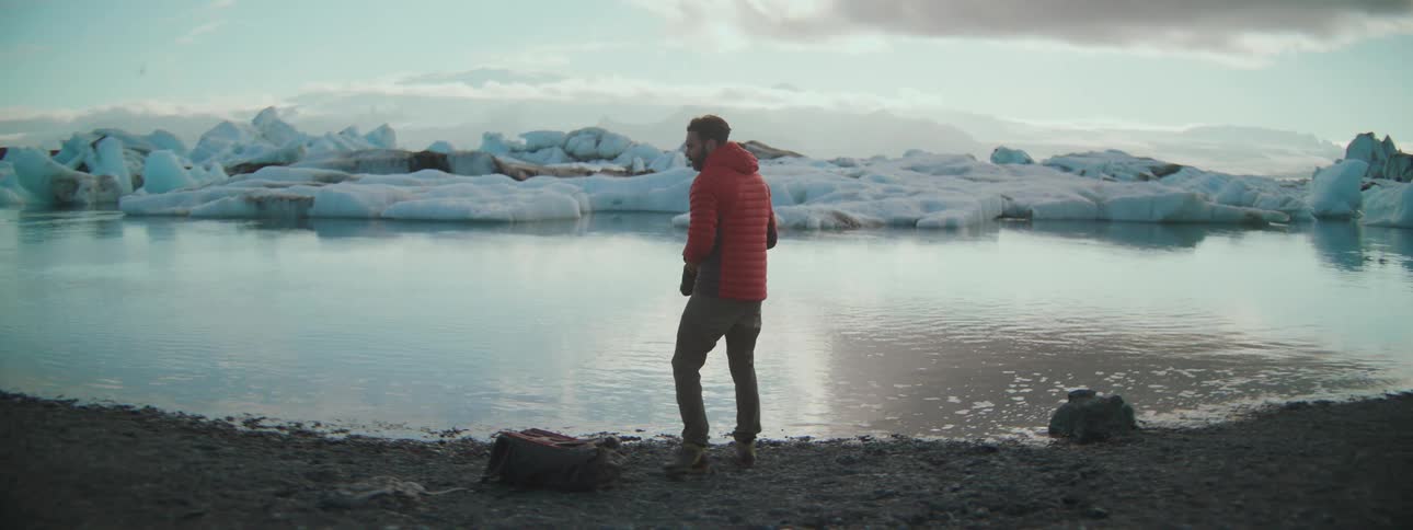 An adventurous photographer in a red jacket takes pictures of a majestic icy lagoon surrounded by glaciers