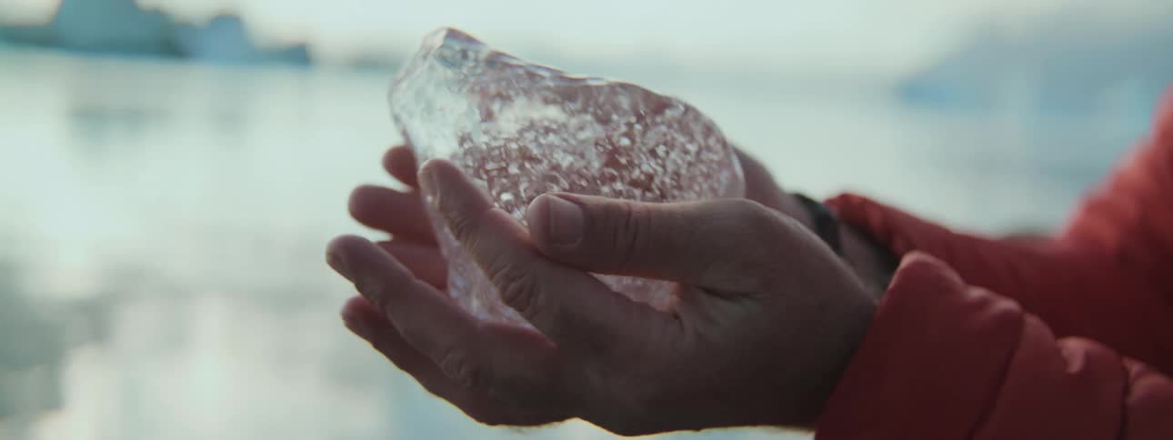 An explorer carefully holds a transparent piece of ancient glacial ice in their hands