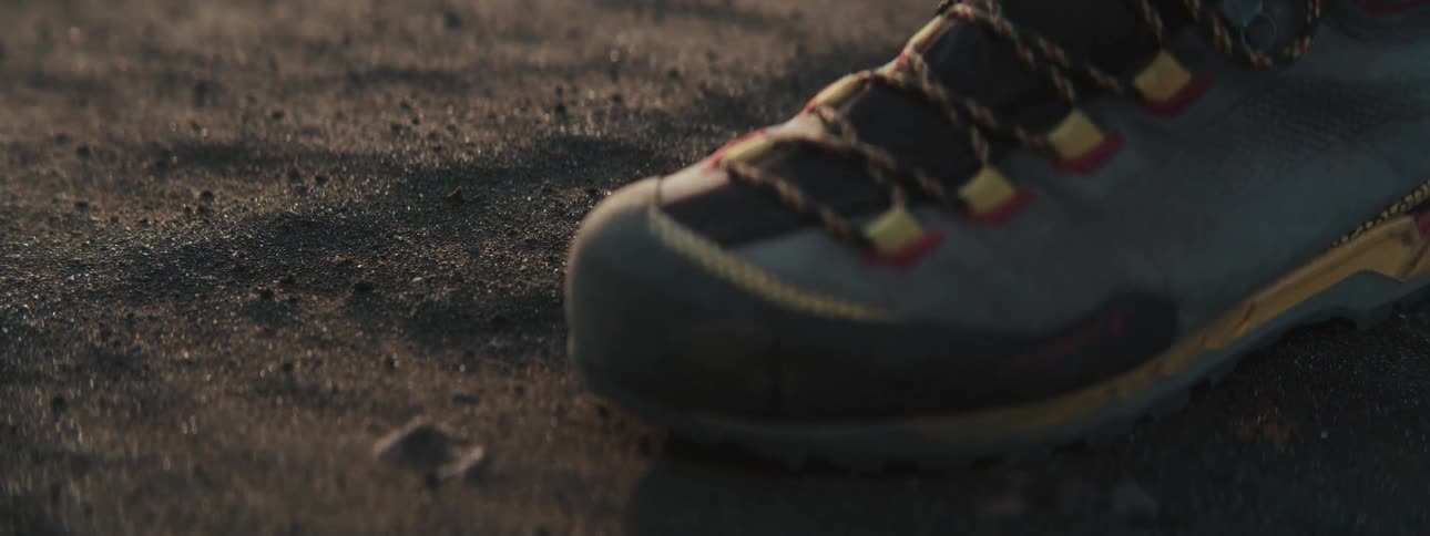 A close-up, slow-motion shot of a hiking boot making an imprint in dark sand