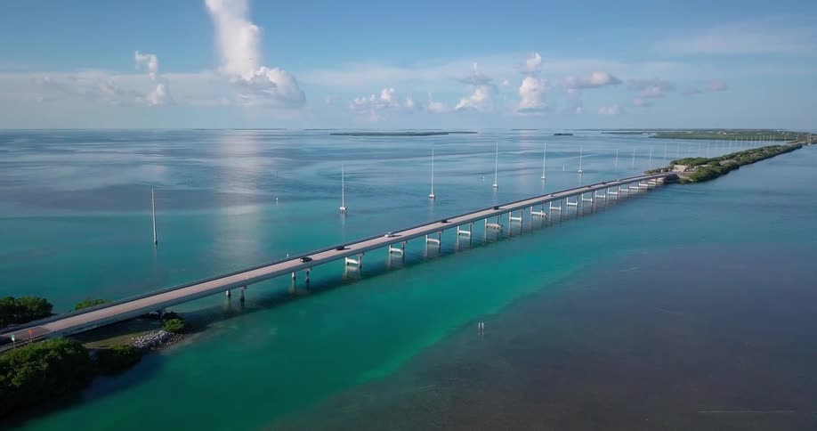 Cars travel on a long bridge over a blue ocean